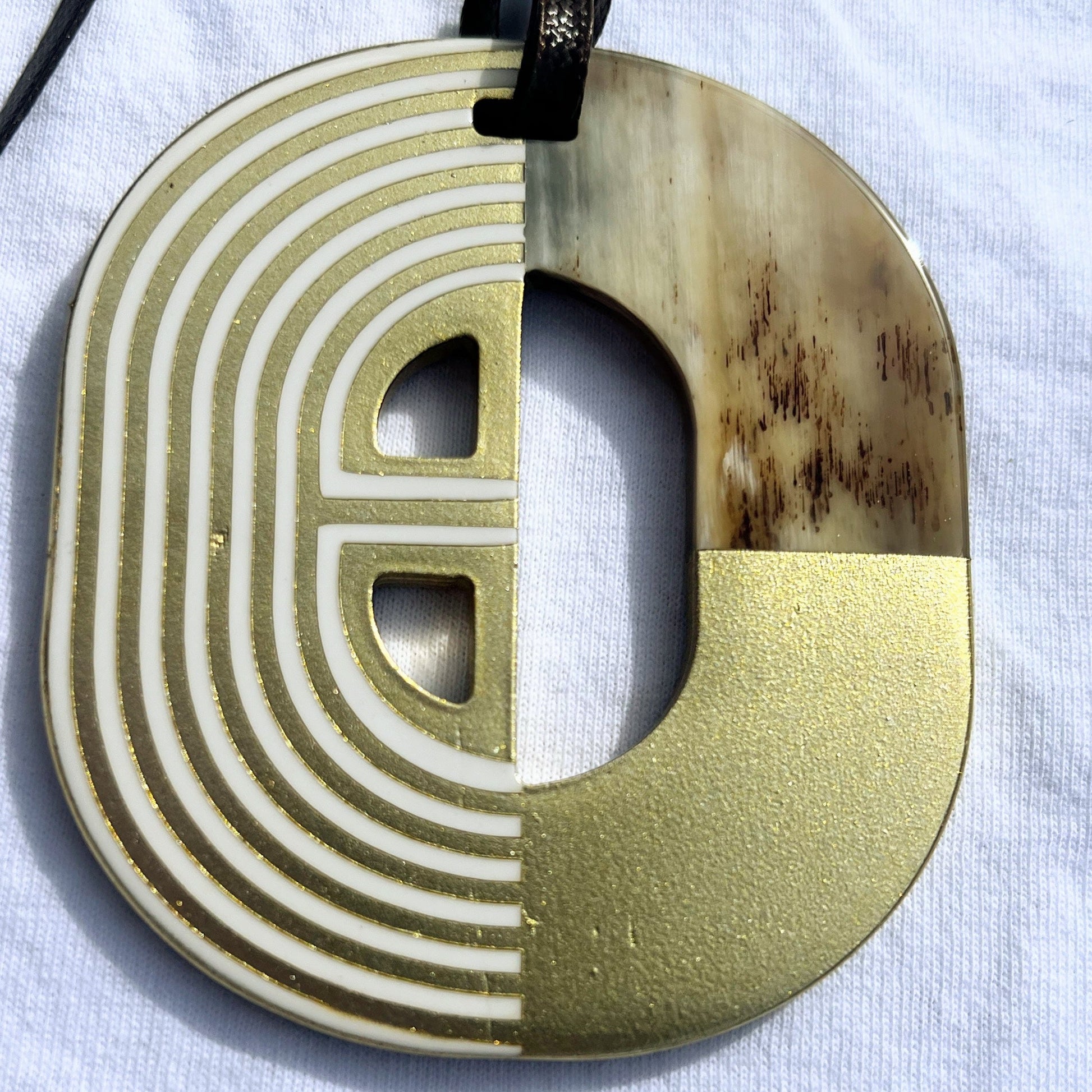  Pendentif en corne naturelle au design graphique bicolore rouge et ivoire. Sa forme semi-circulaire et ses lignes géométriques blanches contrastées apportent une touche d’élégance et de modernité. Il est suspendu à un cordon noir pour un style unique et audacieux.

