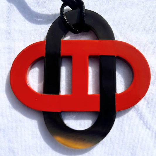 Pendentif en corne naturelle noir et beige au design symétrique inspiré des motifs entrelacés. Son jeu de contrastes entre la corne brute et la partie noire lui confère un style raffiné et intemporel. Il est monté sur un cordon noir ajustable.